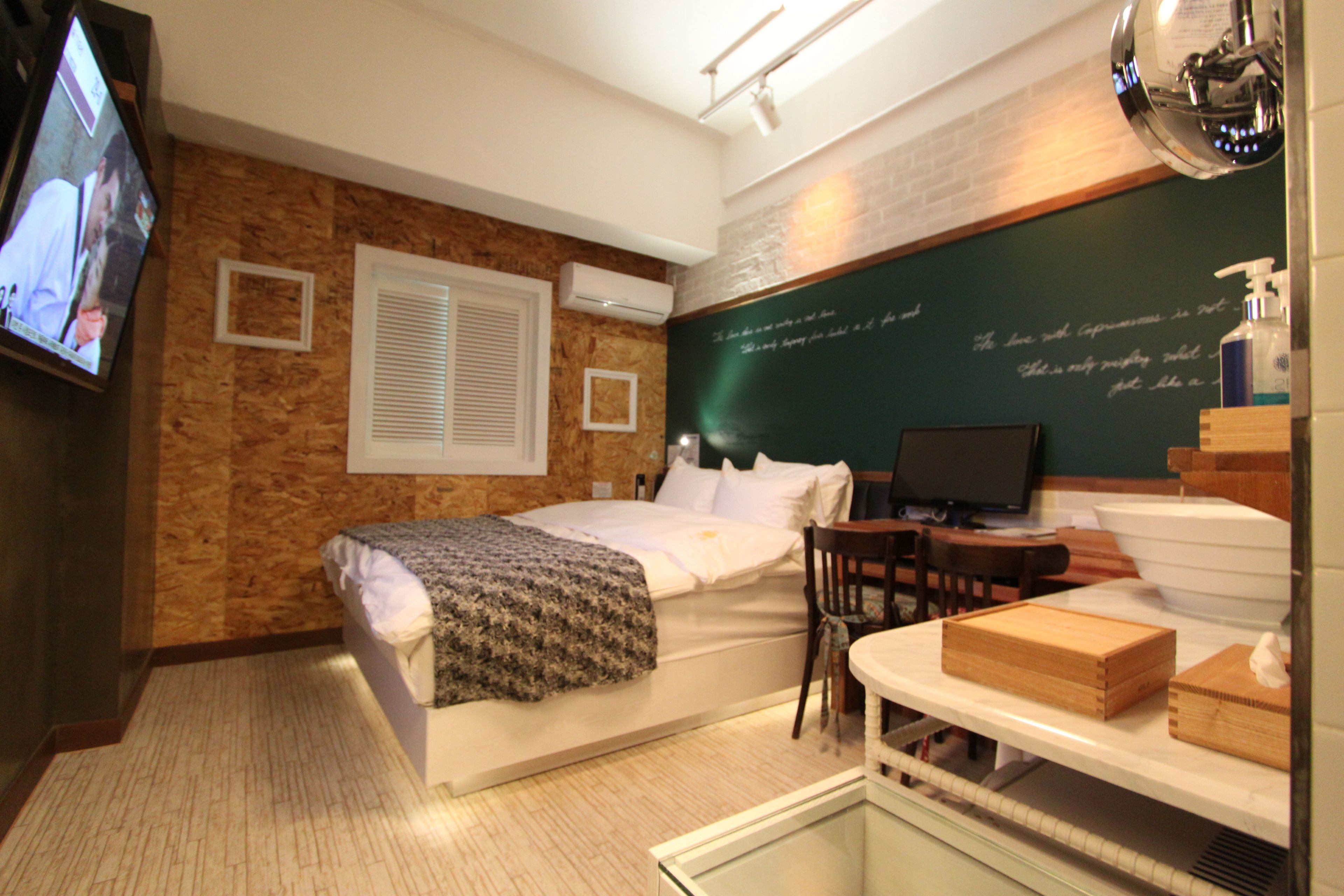 Habitación de hotel con cama, escritorio, silla, televisor y una pizarra con texto.