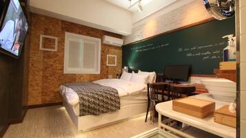 Habitación de hotel con cama, escritorio, silla, televisor y una pizarra con texto.