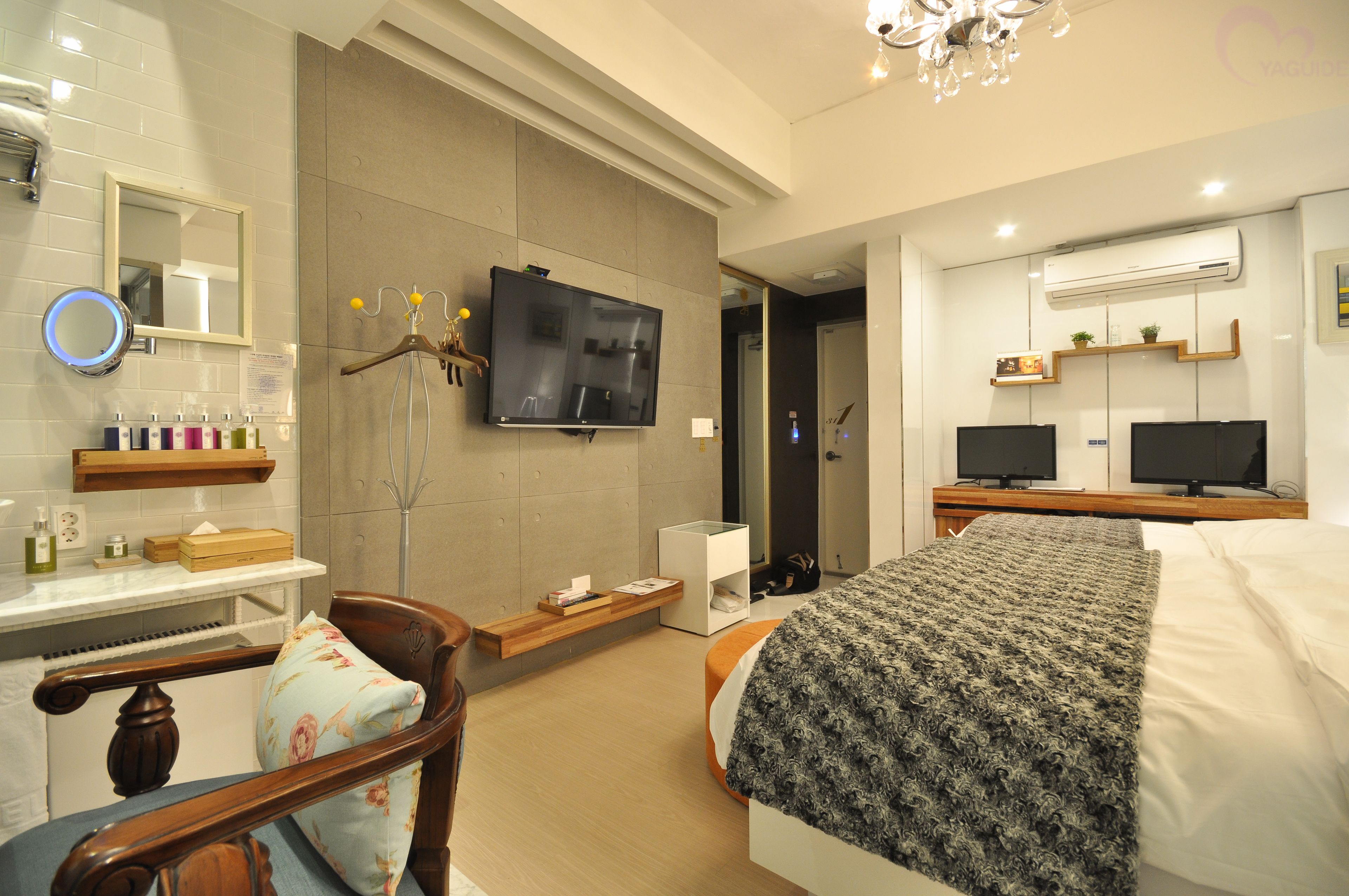 A modern hotel room with a bed, a TV, a desk with a mirror, and a wardrobe.