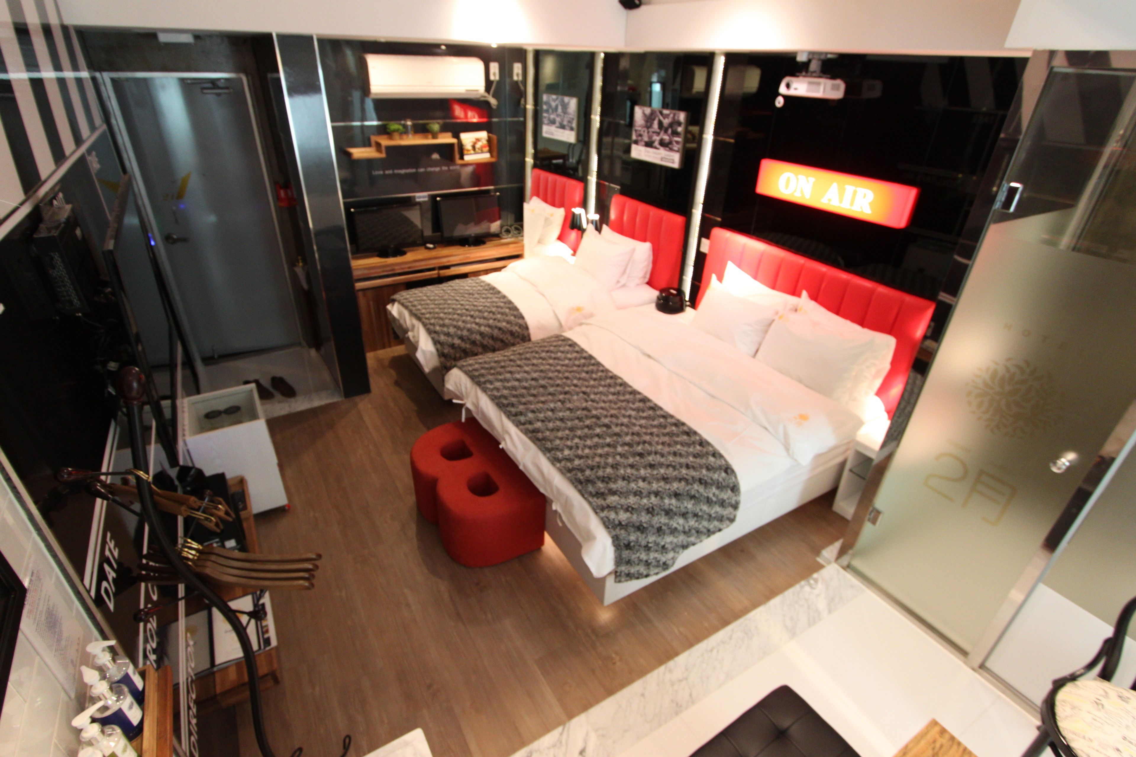 Een moderne hotelkamer met een groot bed, een kleiner bed, een rode stoel, een spiegel en een 'ON AIR' bord.