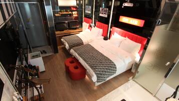 Een moderne hotelkamer met een groot bed, een kleiner bed, een rode stoel, een spiegel en een 'ON AIR' bord.