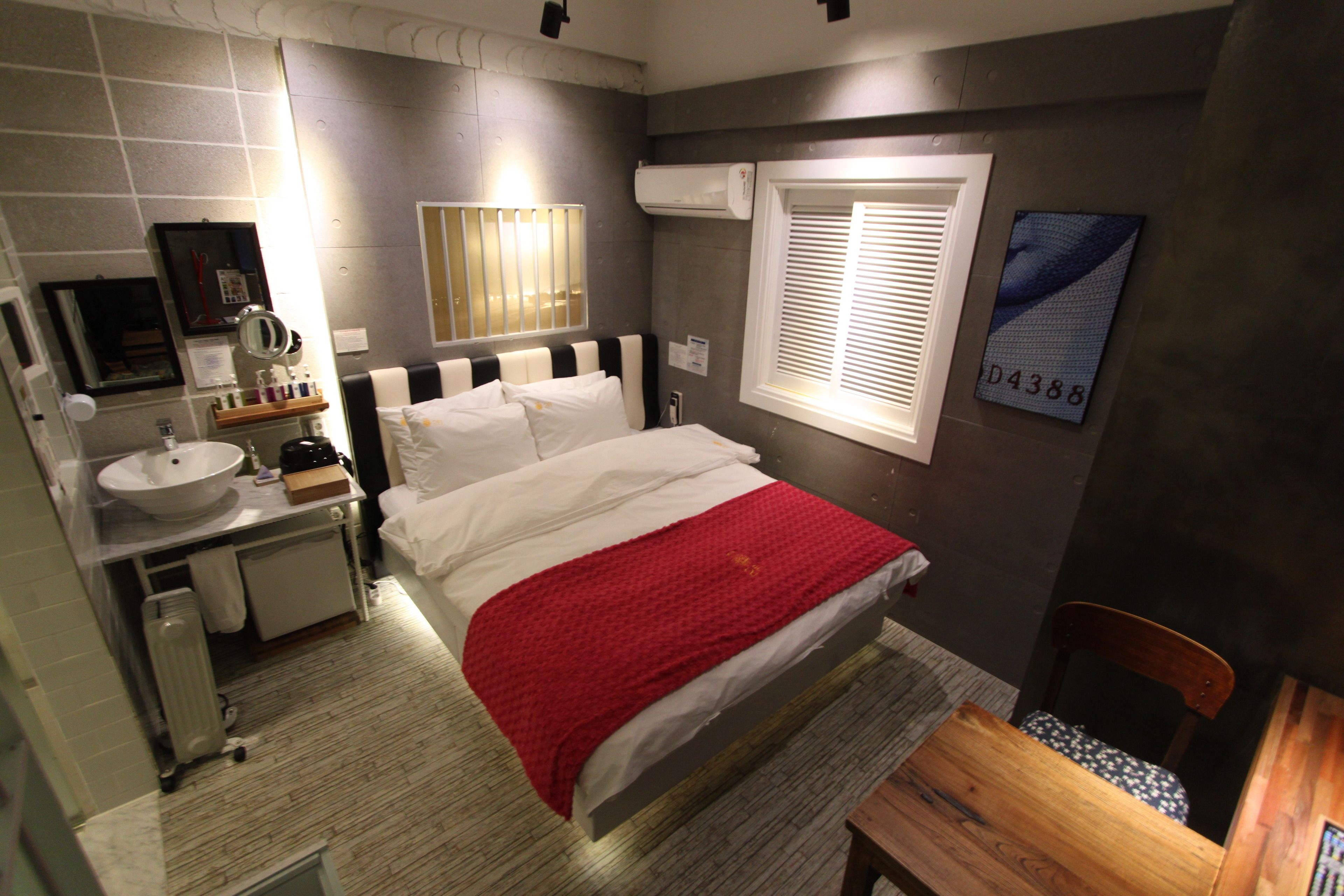 A hotel room with a bed, bedside table, and a window with blinds.