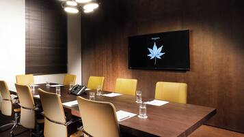 Un salón de conferencias con una larga mesa, sillas amarillas y una pantalla montada que muestra una hoja de arce.