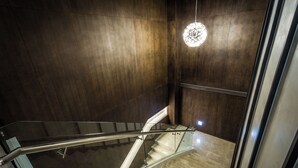 Un interior moderno con barandilla de vidrio, pared de madera y lámpara colgante.