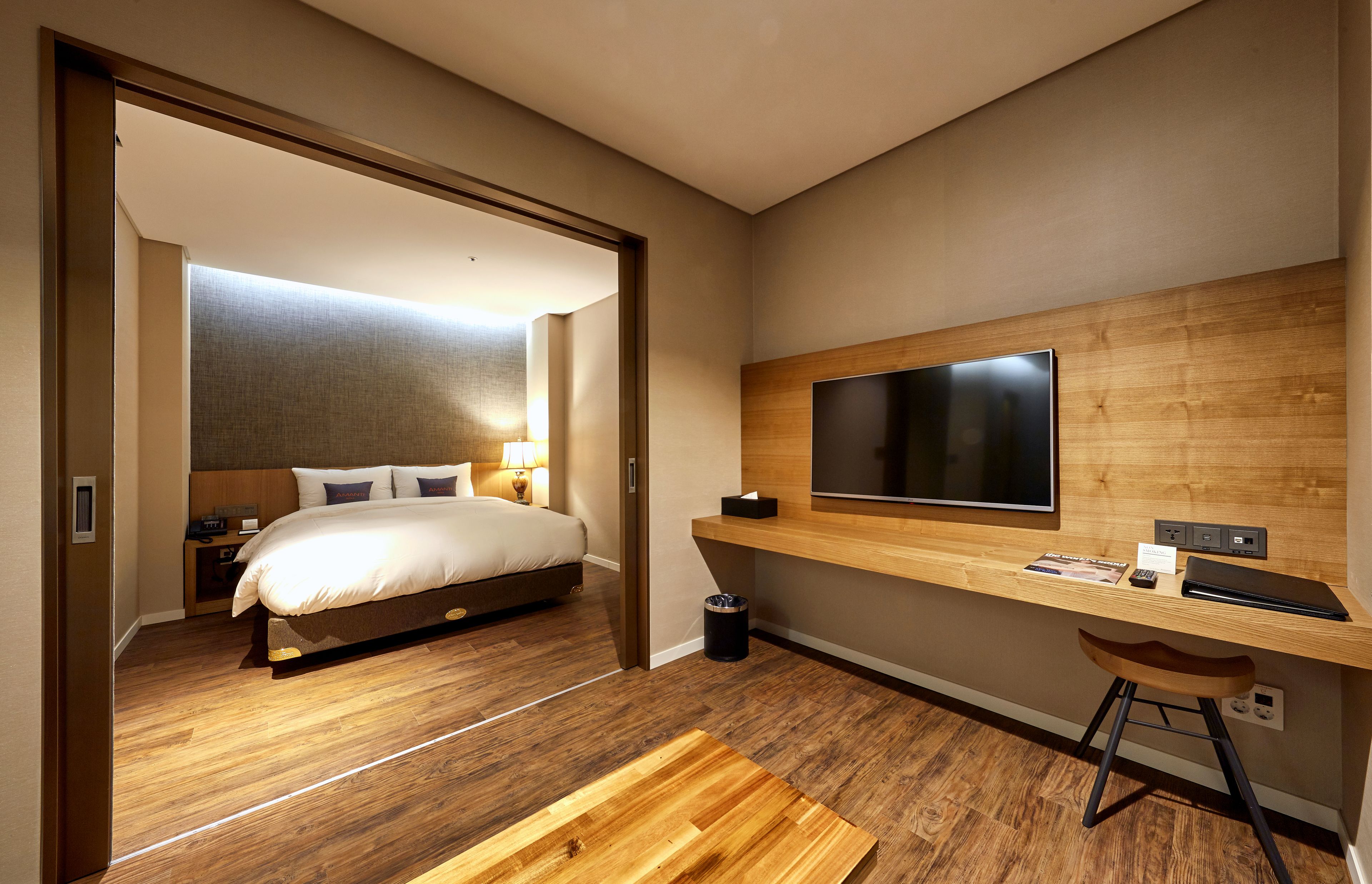 Een moderne hotelkamer met een houten vloer, een groot bed, een bureau met een computer en een aan de muur bevestigde televisie.