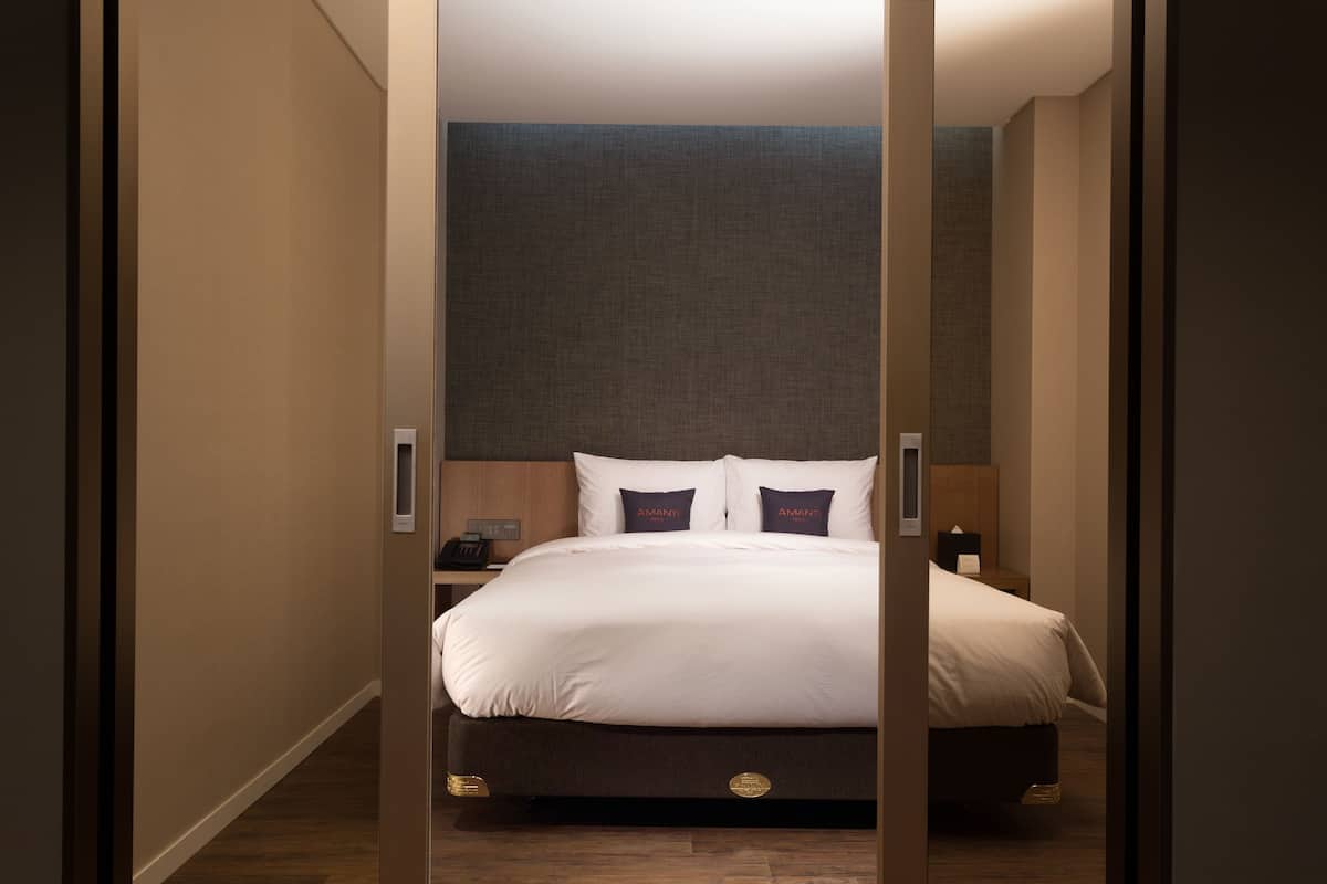 Una habitación de hotel con una cama grande, una mesita de noche y un teléfono instalado en la pared.