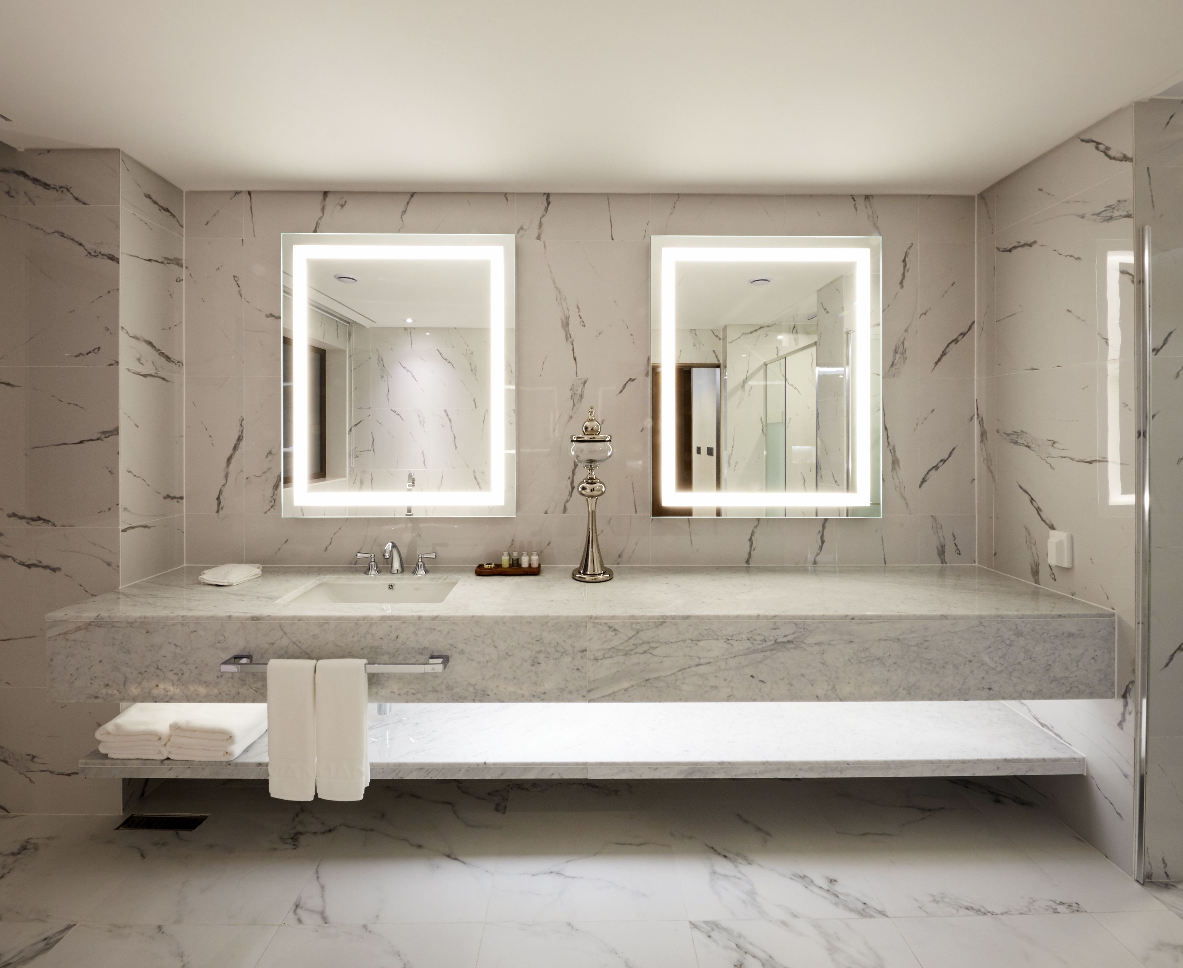 A modern bathroom with two sinks, a large mirror, and a vanity with a towel rack.