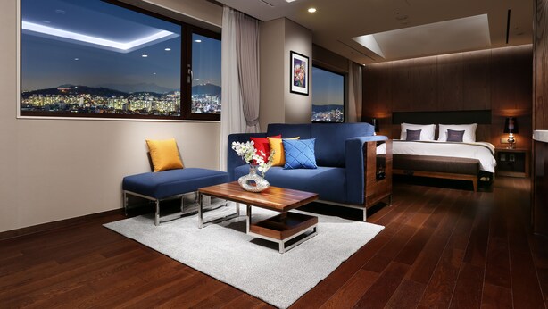 Una habitación de hotel moderna con vista a la ciudad, un sofá, una cama y una pequeña mesa con un florero.