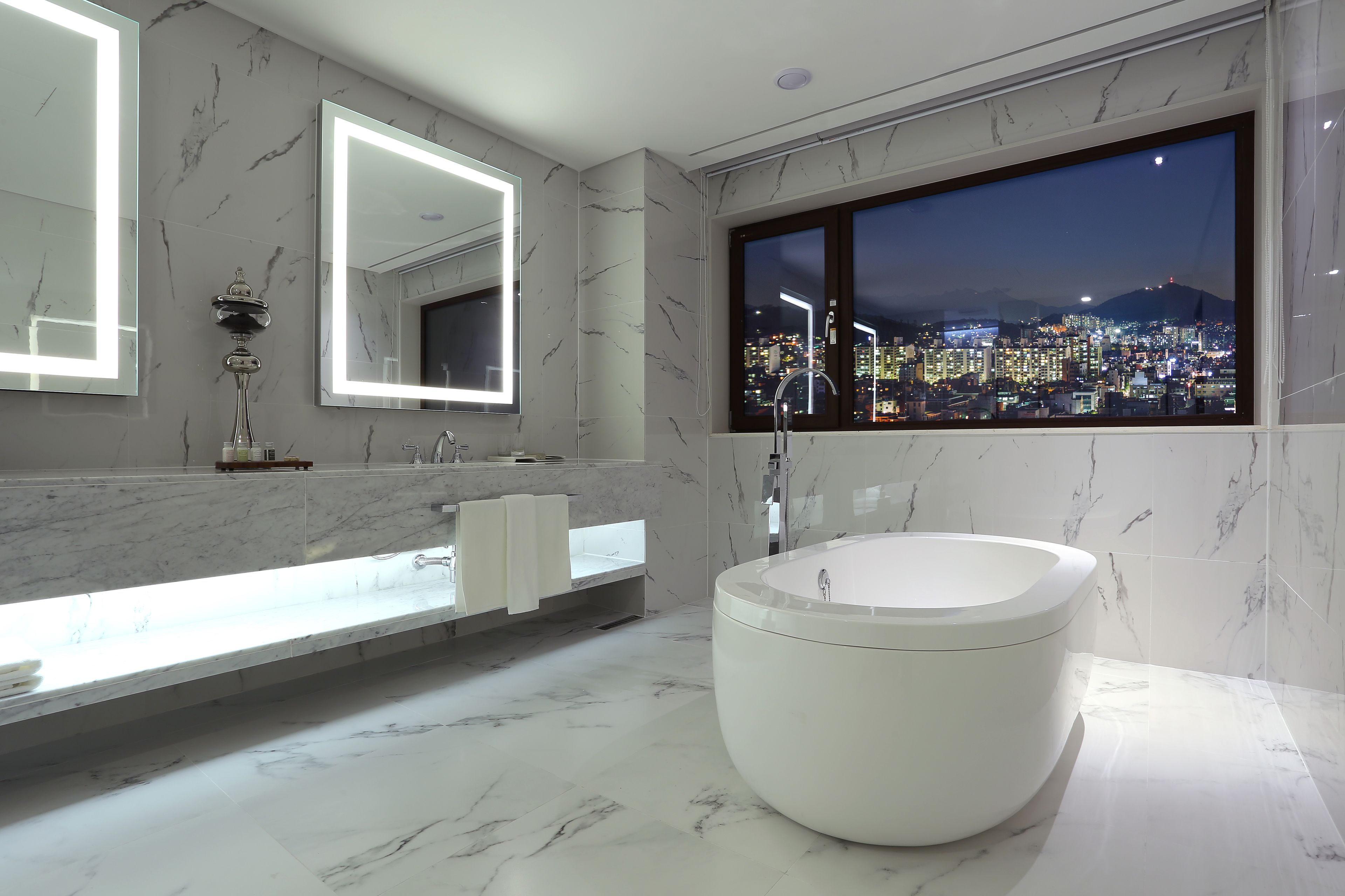 A modern bathroom with a large bathtub, a vanity with a mirror, and a window with a cityscape view.
