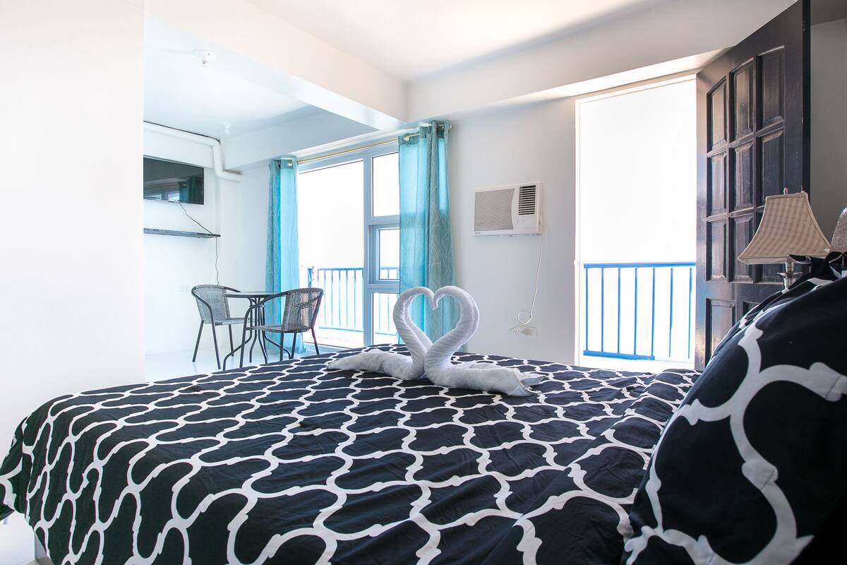 A hotel room with a bed, a balcony, a chair, and a lamp.
