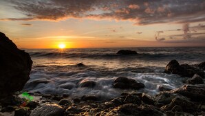 Un atardecer sobre una costa rocosa con olas rompiendo contra las rocas.