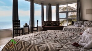 Habitación de hotel con una cama grande, una zona de estar con vista al mar y una mesita con una planta.