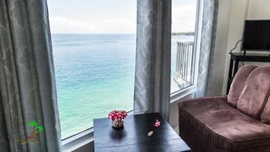Una habitación con vista al mar, un sofá marrón, una mesita con un florero y un televisor sobre un mueble.