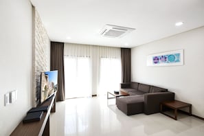A modern living room with a sectional sofa, a flat-screen TV mounted on a brick-patterned wall, a coffee table, and a framed artwork on the wall. - The Soom Forest Hotel (Yongin)