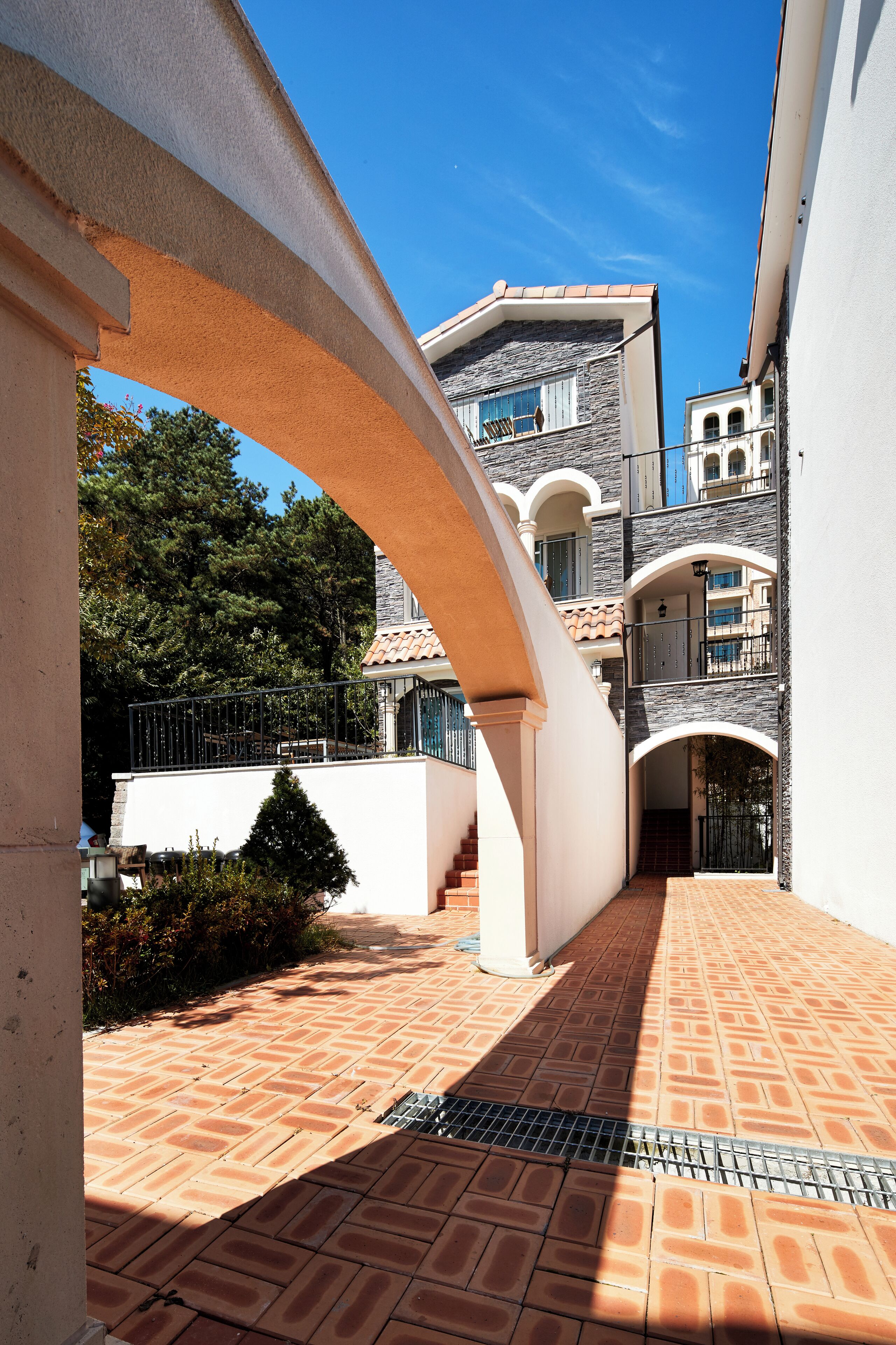 A courtyard with a tiled floor, a stone wall, and a building with a balcony.