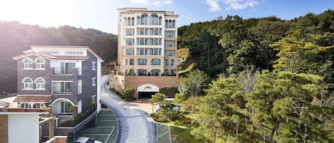 A multi-story building with a central courtyard, surrounded by trees and a hilly landscape.