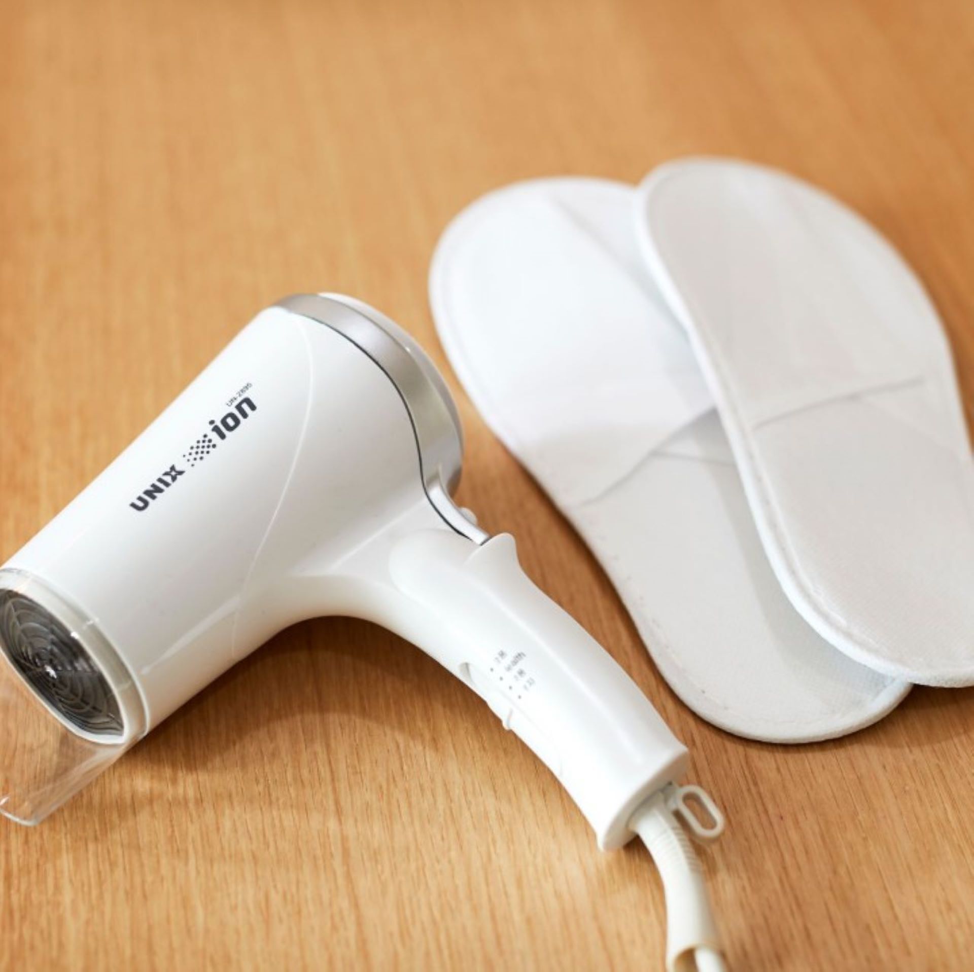 A white hair dryer with a transparent attachment and a white charging cable, placed on a wooden surface.