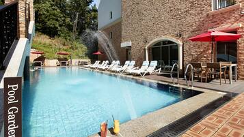 A pool with lounge chairs and umbrellas, a sign reading "Pool Garden," and a water feature.