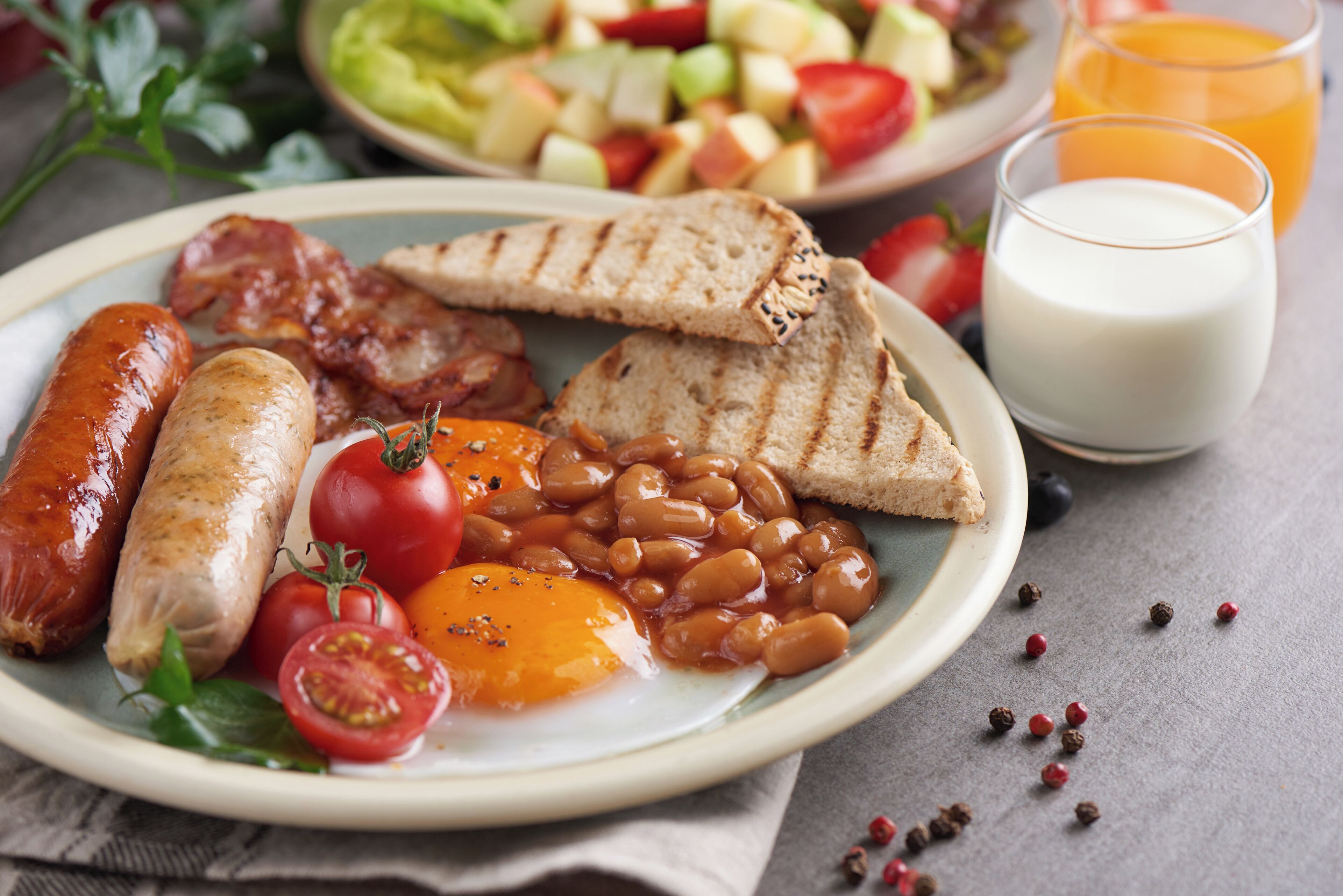 Ein Teller mit Würstchen, Bohnen, Tomaten, Toast und einem Glas Milch.
