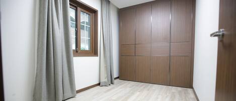 A room with a large window, wooden wardrobe, and light-colored flooring.