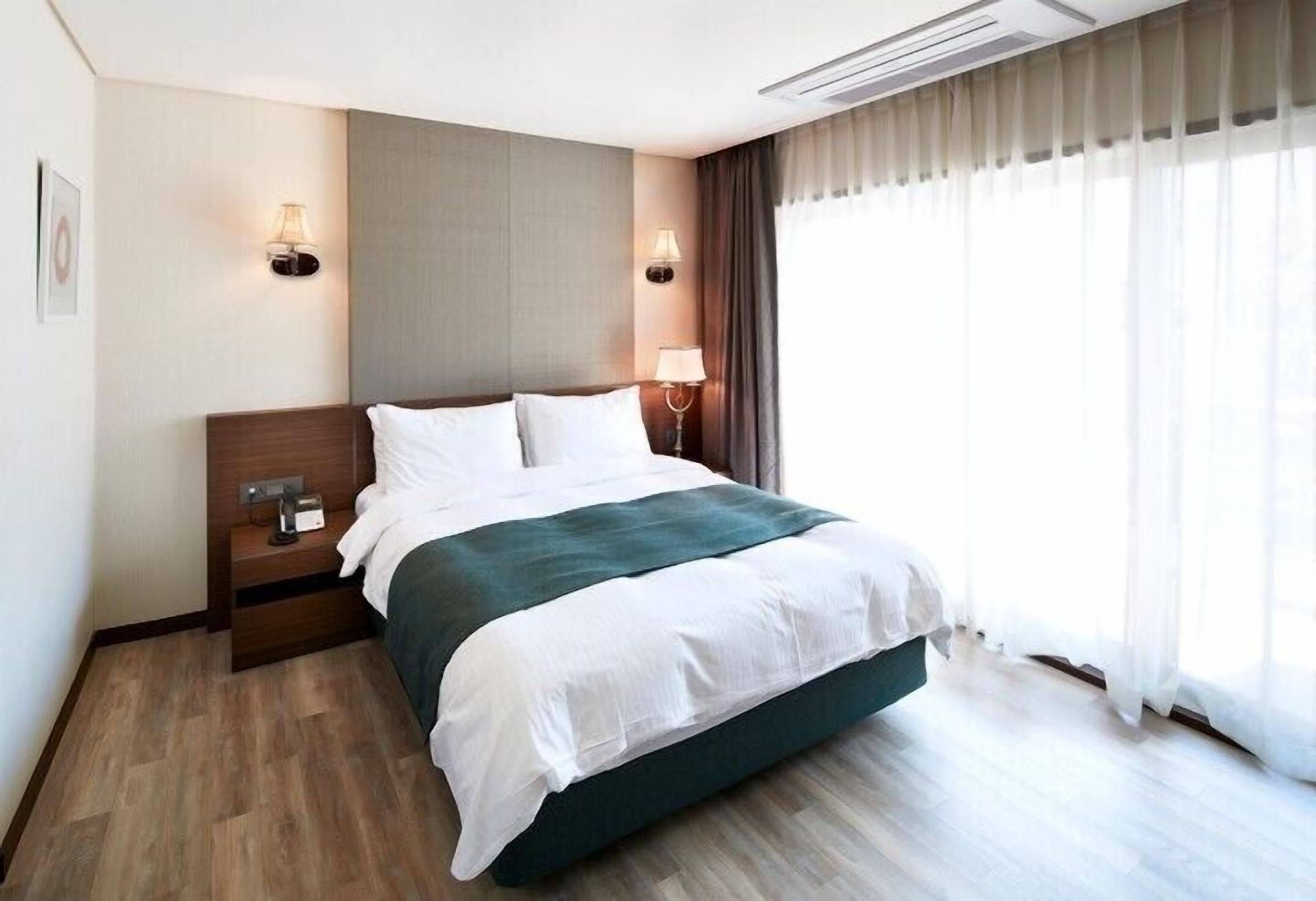 A hotel room with a bed, bedside lamps, a nightstand, and a window with curtains.
