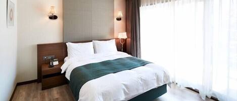 A hotel room with a bed, bedside lamps, a nightstand, and a window with curtains.