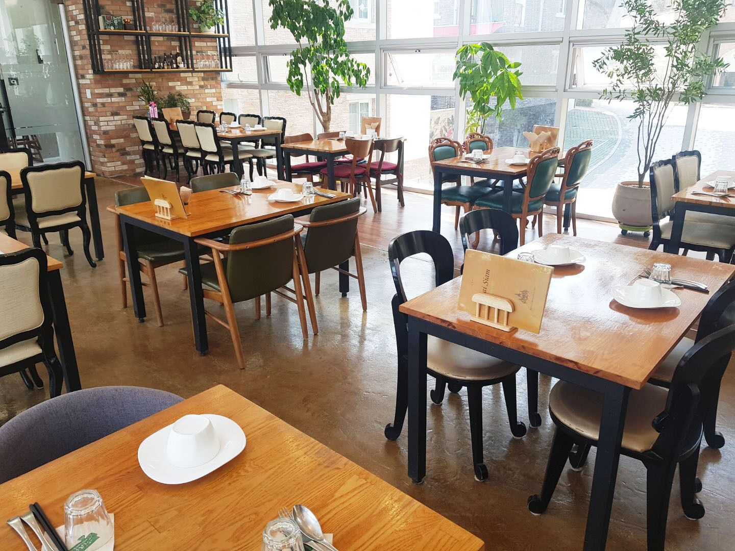 Et restaurantinteriør med flere spiseborde og stole, hvoraf nogle har menukort og bestik.
