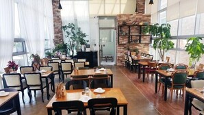 A spacious restaurant with wooden tables and chairs, large windows, and indoor plants. - The Soom Forest Hotel (Yongin)