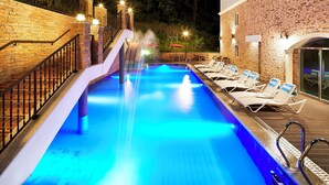 A swimming pool with a water slide, lounge chairs, and a brick wall. - The Soom Forest Hotel (Yongin)