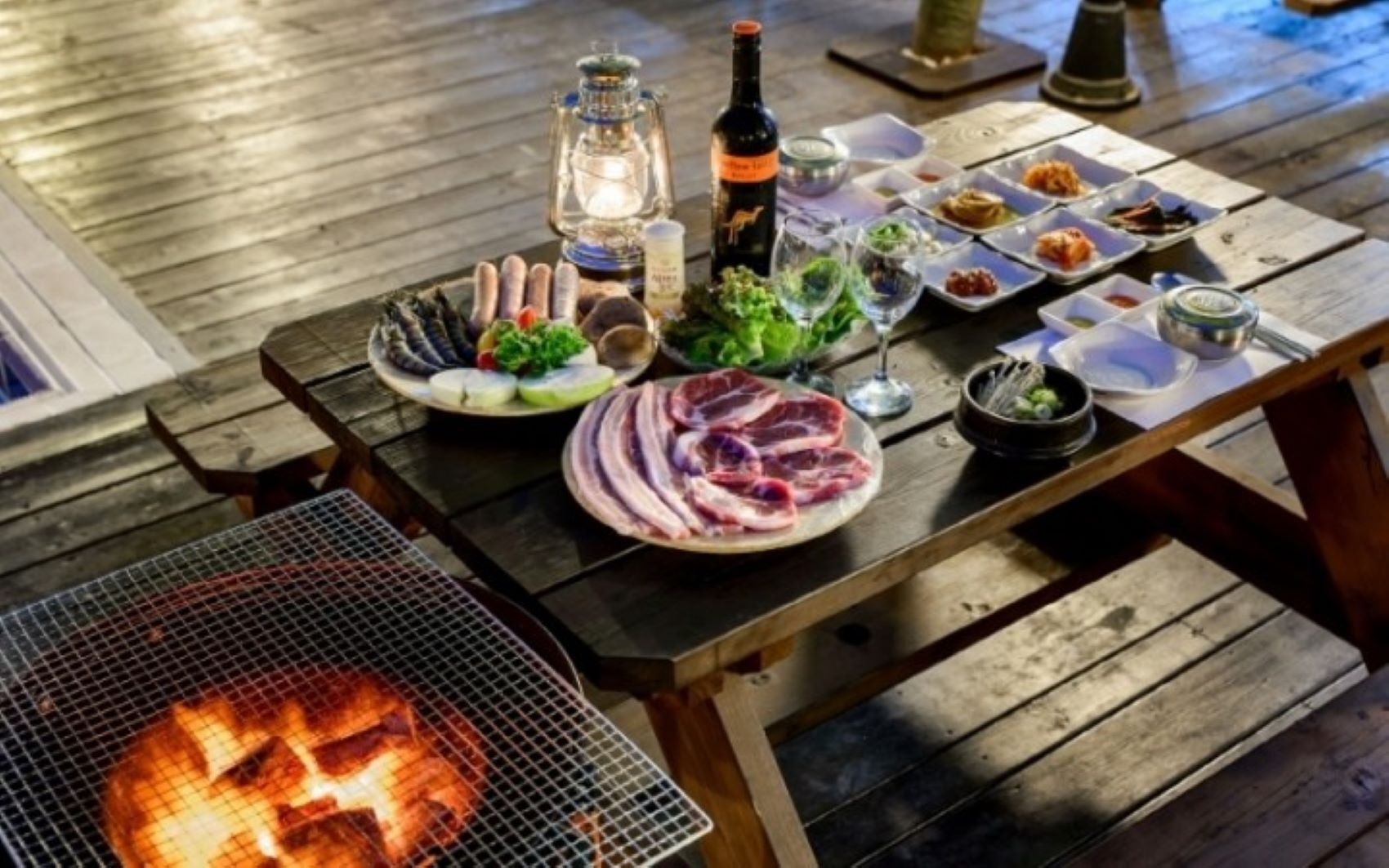 A wooden table set with various dishes, a bottle of wine, and a lantern.