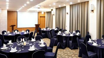 A conference room with round tables, dark blue chairs, and a projector screen.
