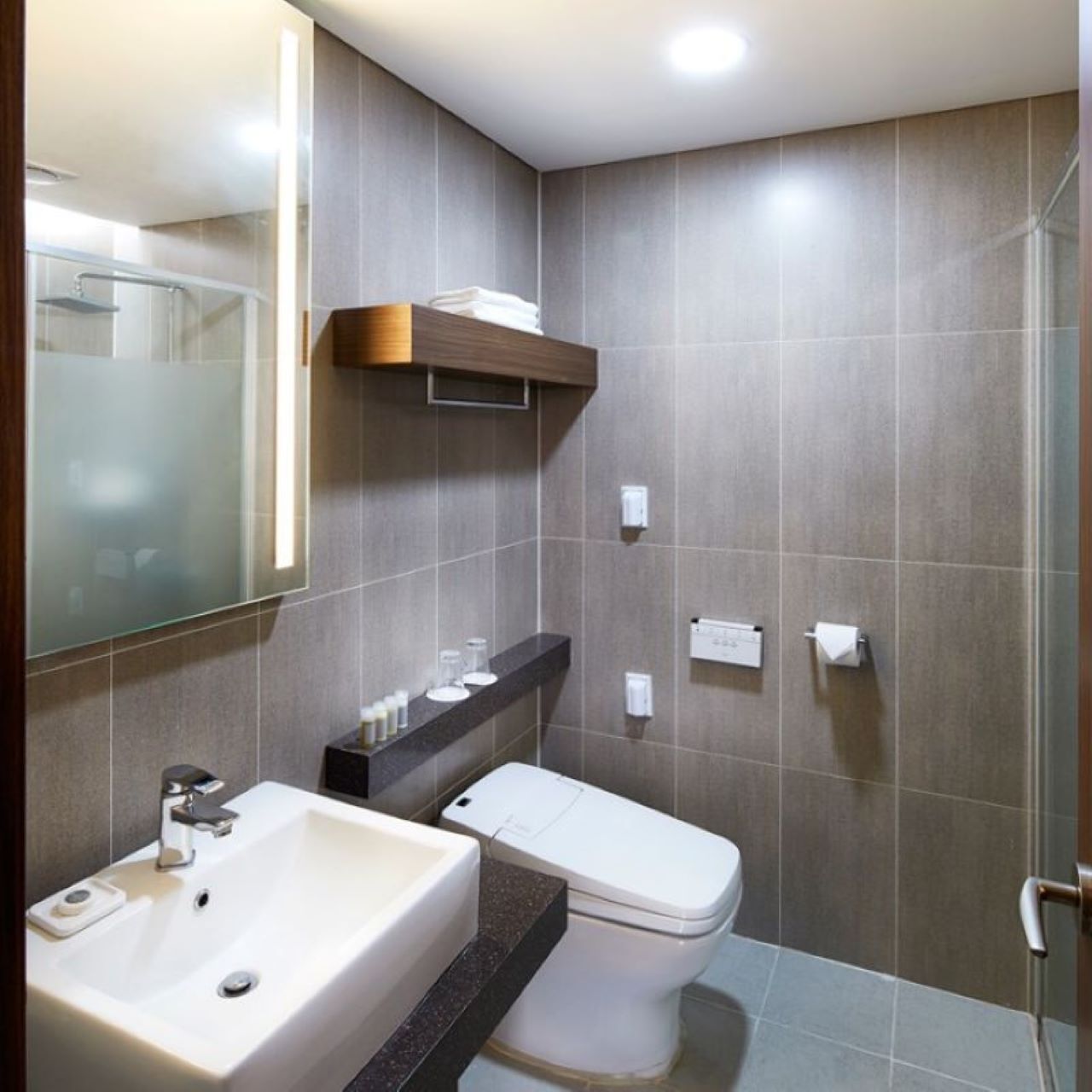 Un baño moderno con un espejo grande, un lavamanos, un inodoro y una zona de ducha.