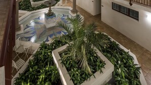 Un atrium à plusieurs niveaux, doté d’une cour centrale agrémentée d’une fontaine, de plantes en pot et d’un sol carrelé.