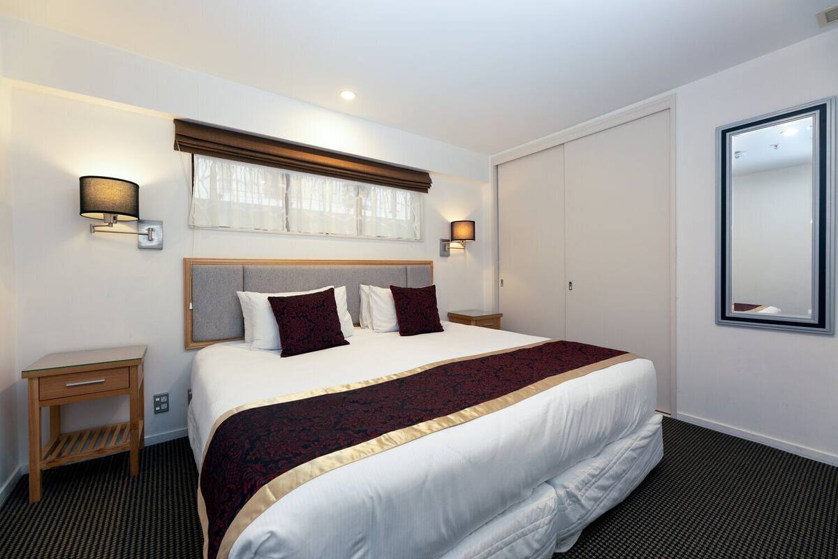 A hotel room with a large bed, bedside lamps, a small bedside table, a wardrobe, and a large mirror.