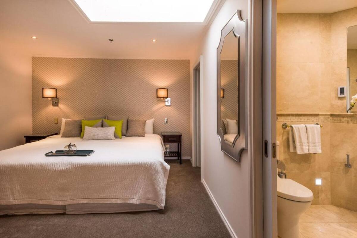 A hotel room with a large bed, two bedside lamps, a nightstand, a mirror, and a view of the bathroom.