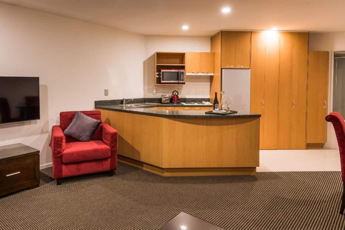 A modern kitchen with a built-in microwave, a refrigerator, and a coffee maker. There is a red chair and a wooden cabinet in the room.