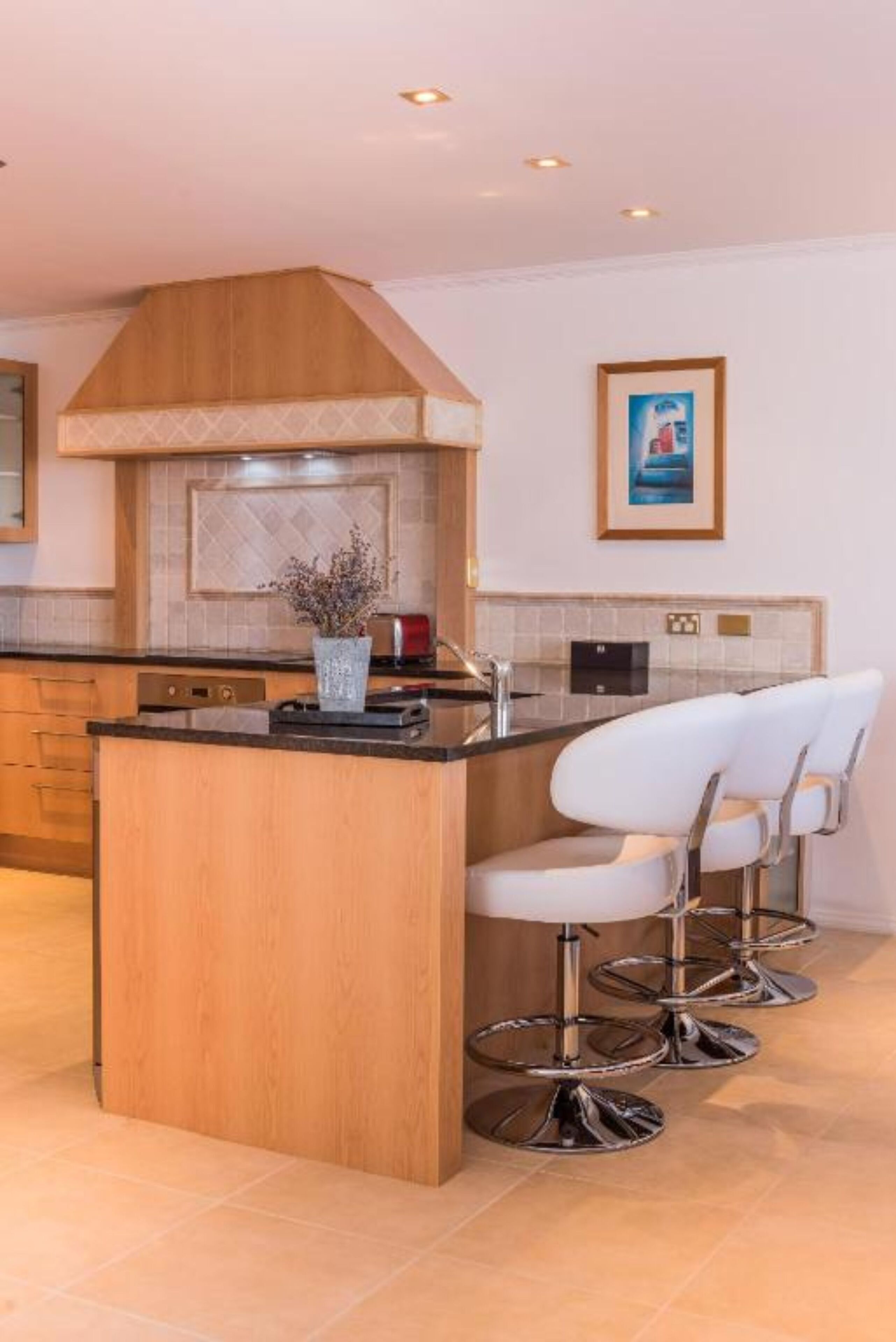 Une cuisine moderne avec un îlot central en bois, des tabourets de bar et un mur recouvert de carreaux.