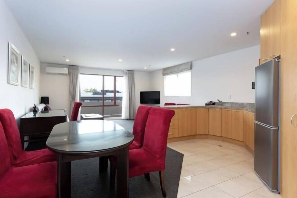 A modern kitchen with a dining area, a TV, and a large window.