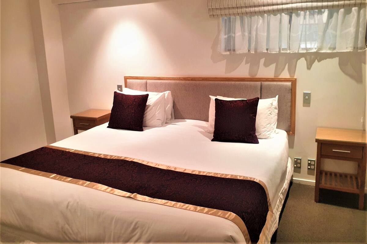 A neatly made bed with a headboard, two bedside tables, and a window with curtains.