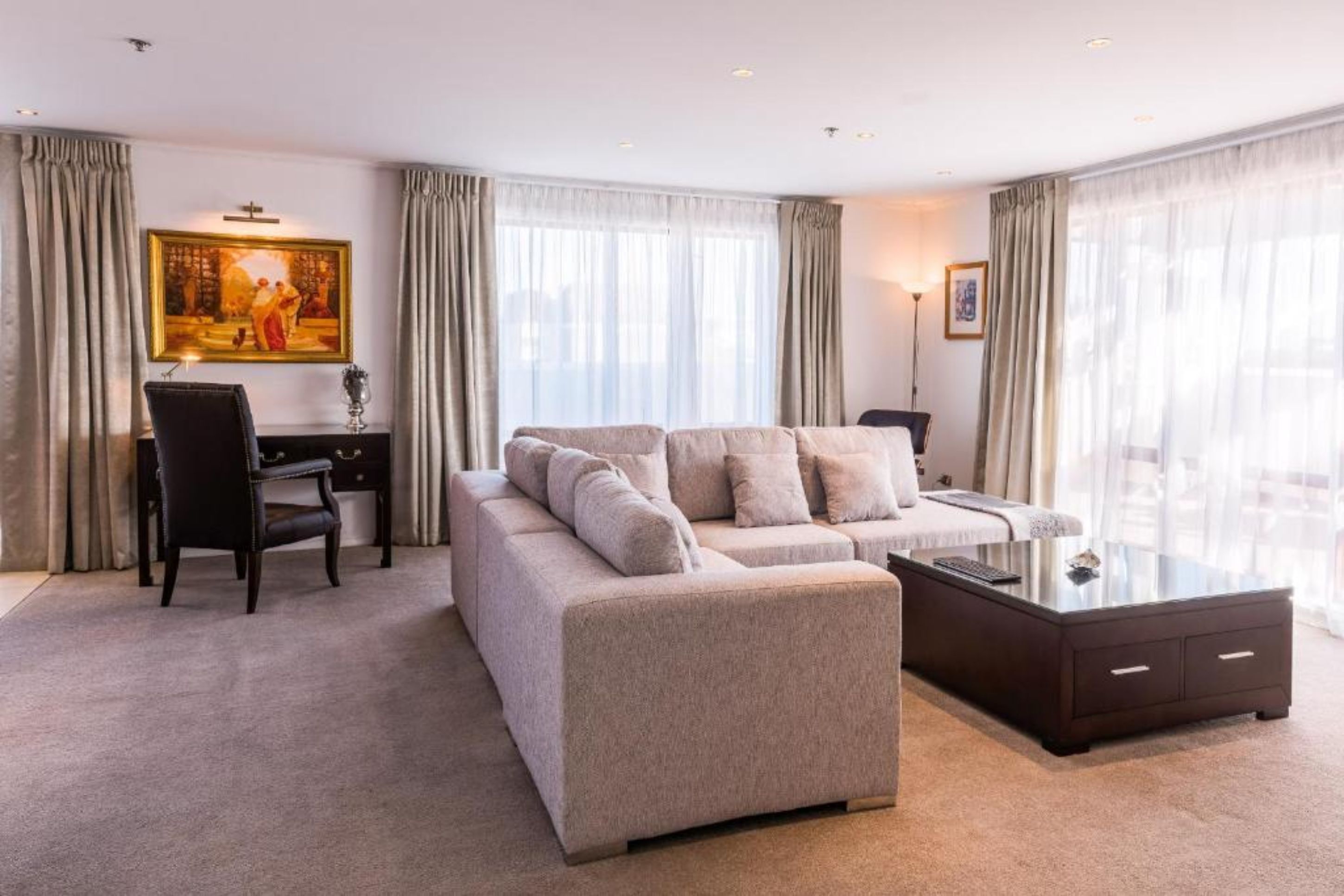 Una sala de estar moderna con un sofá color beige, una mesa de centro de vidrio y un escritorio con una silla.