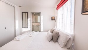 Une chambre à coucher avec un grand lit, un miroir, une fenêtre avec des rideaux rouges et un luminaire fixé au mur.