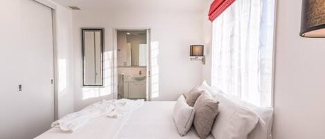 Un dormitorio con una cama grande, un espejo, una ventana con cortinas rojas y una lámpara de pared.