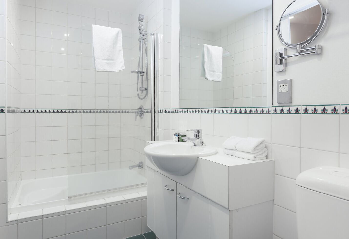 A modern bathroom with a bathtub, a sink, and a toilet. There is a showerhead above the bathtub and a mirror above the sink.