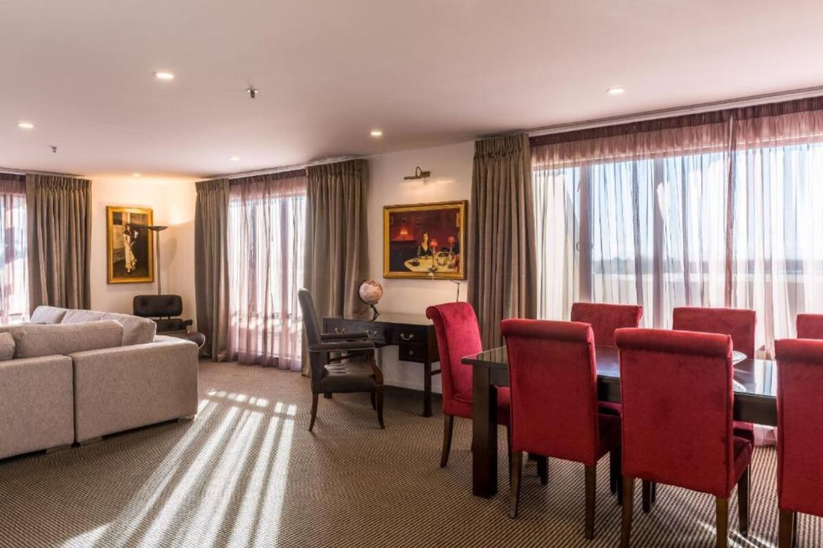 A hotel room with a sofa, dining table with chairs, a desk with a chair, and a globe.