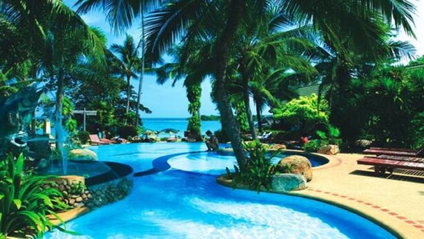 Ein tropisches Resort mit Swimmingpool, umgeben von Palmen und Liegestühlen.