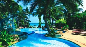 Ett tropiskt semesterparadis med en pool omgiven av palmer och solstolar.