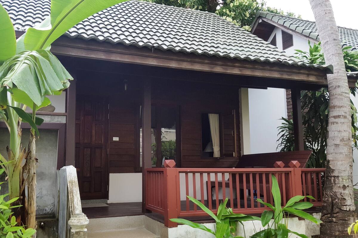 Une maison en bois avec un toit en tuiles, une véranda dotée d’une balustrade et une porte.