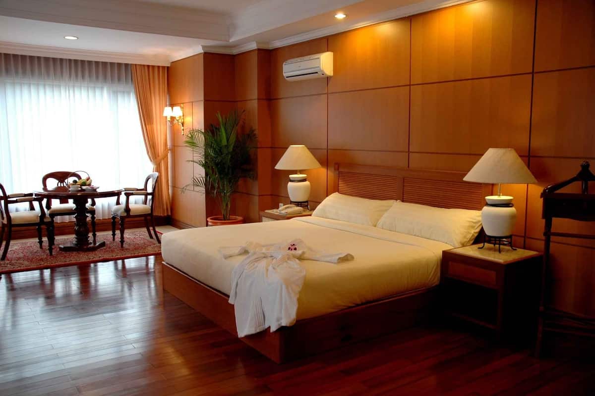 Quarto de hotel com uma cama grande, duas mesas de cabeceira com luminárias, uma escrivaninha com cadeira e um vaso de planta.