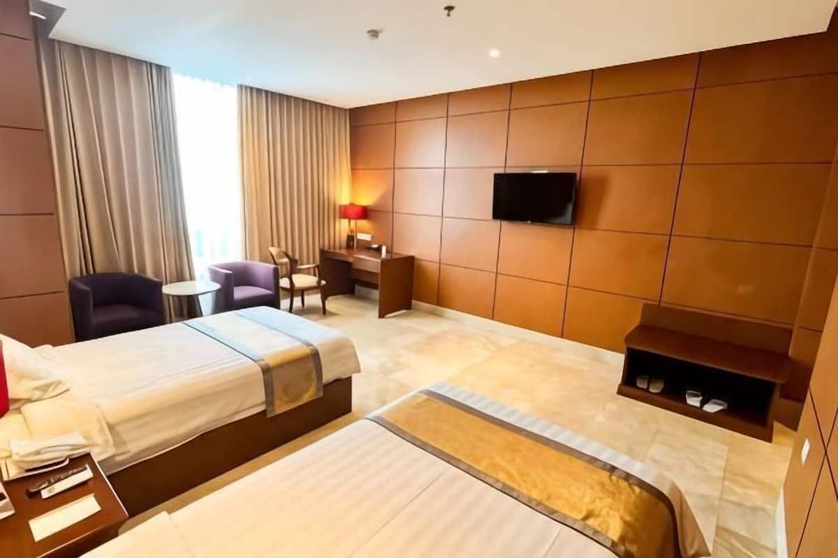 Quarto de hotel com duas camas, uma escrivaninha, uma cadeira, televisão e uma janela grande com cortinas.