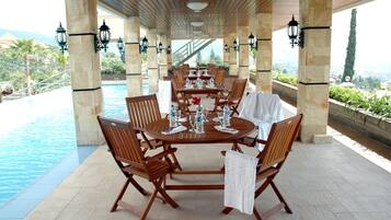 Un área de comedor al aire libre techada con vista a la piscina, que incluye una mesa redonda con sillas y mantel blanco.